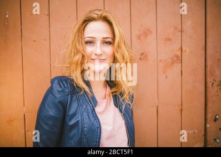 Femme caucasienne modèle avec cheveux de gingembre posant sur fond de bois. Portrait d'une jeune fille tendre à la tête rouge avec une peau saine et téméraire regardant l'appareil photo Banque D'Images