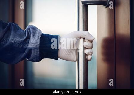 La main mâle dans le gant en latex blanc maintient la poignée lors de l'ouverture de la porte. Concept de pandémie COVID-19. Banque D'Images