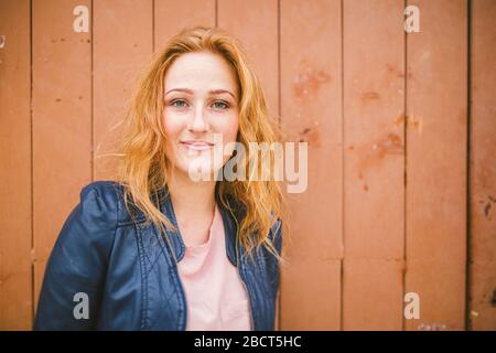 Gros plan portrait de charmante jeune femme blanche à tête rouge avec de mignons freckles gaiement tout en se tenant sur un mur de bois. Femme freckled à tête rouge Banque D'Images