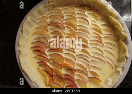 les tranches de pommes dans des rangées nettes sur le gâteau sous la forme de cuisson en céramique recouverte d'une fine couche de glacer avant de les mettre dans un four. Banque D'Images