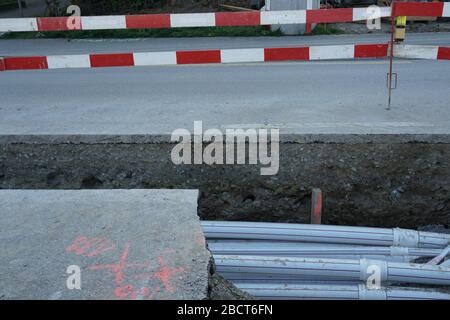 tuyaux épais en polypropylène dans un puits de construction dans une rue soigneusement taillé en asphalte, c'est un chantier de génie civil avec des planches à barrières rouge-blanc Banque D'Images