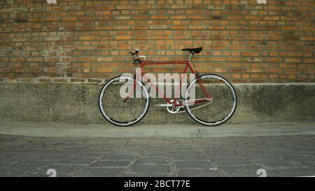 Vélo à engrenage fixe Singlespeed rouge de style rétro isolé sur un mur de briques Banque D'Images