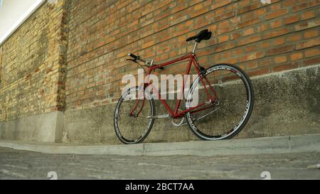 Vélo à engrenage fixe Singlespeed rouge de style rétro isolé sur un mur de briques Banque D'Images