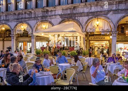 Les personnes assis à l'extérieur du Caffè Lavena sur la place St Marc en début de soirée à l'écoute du groupe de musiciens, Venise, Italie Banque D'Images