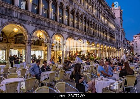 Les personnes assis à l'extérieur du Caffè Lavena sur la place St Marc en début de soirée à l'écoute du groupe de musiciens, Venise, Italie Banque D'Images