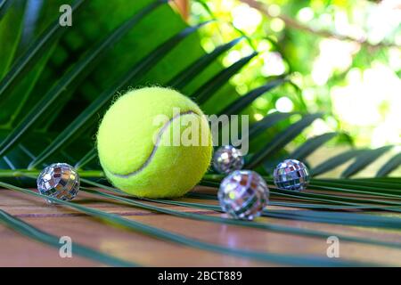 Aménagement de tennis avec balle de tennis et boules de discothèque sur fond de feuilles de palmier tropicales. Concept de fête du sport. Plat, vue de dessus, mise au point sélective. Banque D'Images