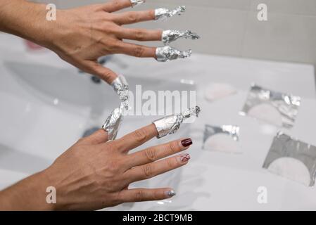 Mains enveloppées dans du papier aluminium avec de l'acétone pour éliminer les traces de peinture à l'ongle. Banque D'Images