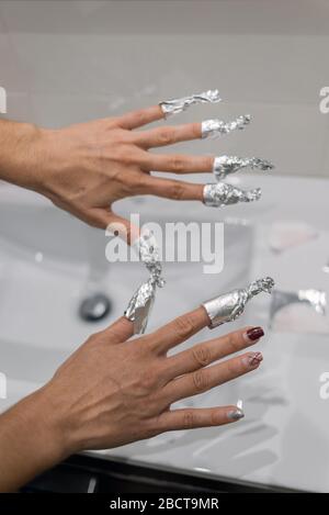 Mains enveloppées dans du papier aluminium avec de l'acétone pour éliminer les traces de peinture à l'ongle. Banque D'Images