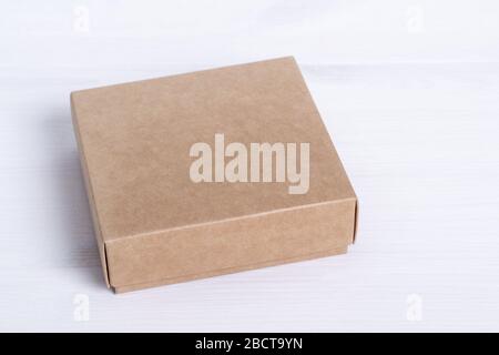 Boîte en carton vierge isolée sur fond de bois blanc. Vue latérale de la boîte en papier pour l'artisanat. Petit carton carré fermé. Emballage écologique d'expédition Banque D'Images