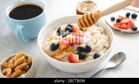 Ajouter du miel au porridge de flocons d'avoine avec des berries d'été fraîches Banque D'Images