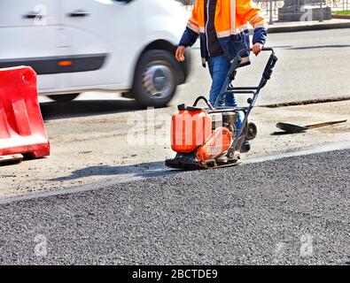 Un travailleur routier compacte l'asphalte sur la chaussée avec un compacteur vibrant à essence. Banque D'Images