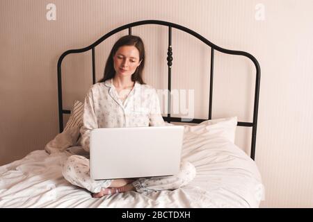 Belle jeune fille adorant à la maison tenant l'ordinateur portable dans la fermeture de lit. Regarder le bureau. Étude à distance. Bonjour. Santé. Banque D'Images