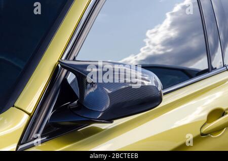 partie d'une voiture de sport chère. miroir carbone. voiture de couleur dorée. sur la fenêtre de porte le reflet du ciel Banque D'Images