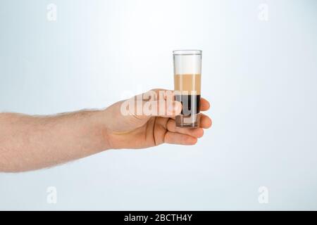 Gros plan d'une main tenant un verre de cocktail en forme de b52 sur fond blanc avec espace de copie.