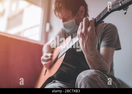 Homme jouant de la guitare acoustique dans la maison quarantaine auto-isolation pendant l'éclosion de coronavirus Covid-19 Banque D'Images