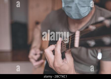 Homme jouant de la guitare acoustique dans la maison quarantaine auto-isolation pendant l'éclosion de coronavirus Covid-19 Banque D'Images