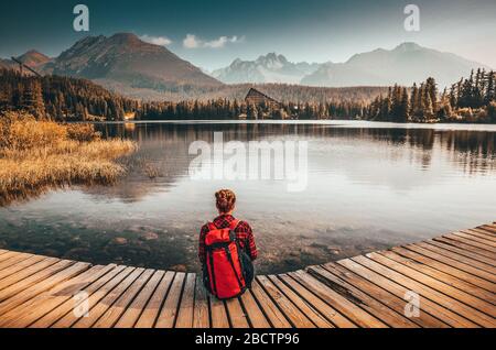 Belle jeune fille assise près d'un lac clair sous de merveilleuses montagnes dans les Hautes Tatras - Slovaquie. Lumière du matin sur le lac Strbske pleso. Photo avant Banque D'Images