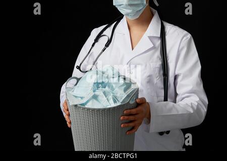 Le médecin tient un seau rempli de masques faciaux usagés, les jetant comme symbole de fin d'épidémie Banque D'Images