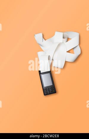 Terminal de carte de crédit sans fil POS pour les paiements et les bandes d'argent à long rouleau sur un fond orange. Banque D'Images