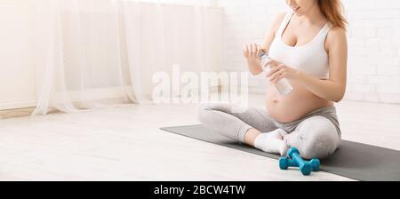 Jeune femme enceinte qui boit de l'eau en position lotus Banque D'Images