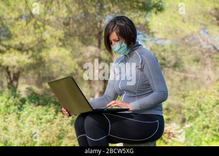 Fille pendant le coronavirus dans un masque à un ordinateur sur la nature. Isolement social. Banque D'Images