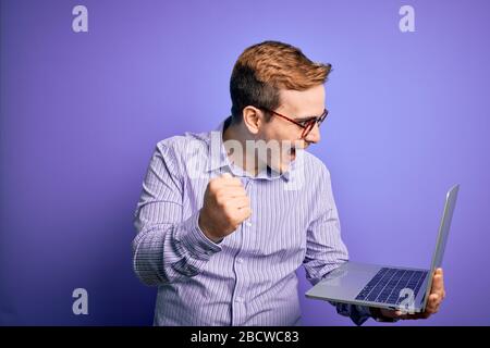 Jeune homme d'affaires à tête rouge travaillant avec un ordinateur portable sur fond mauve criant fier et célébrant la victoire et le succès très excité, encourager Banque D'Images