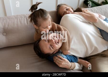 Joyeuses petites soeurs se moquant de rire le père, se reposant sur un canapé. Banque D'Images