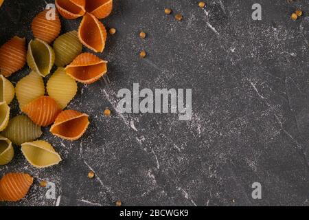 Pâtes Conchiglie Rigate, mélange de coquillages colorés non cuits dispersés sur la table, a laissé un espace vide. Cuisine italienne texturée concept de fond. Haut Banque D'Images