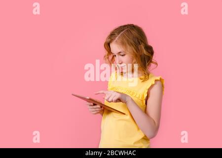 Une adolescente fait ses devoirs sur un comprimé. L'étudiant travaille et communique avec ses amis. Isoler sur un fond rose. Banque D'Images