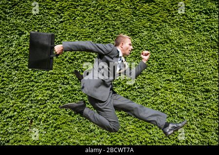 Portrait d'un homme d'affaires sautant à l'extérieur devant un mur d'espace vert vif de copie Banque D'Images