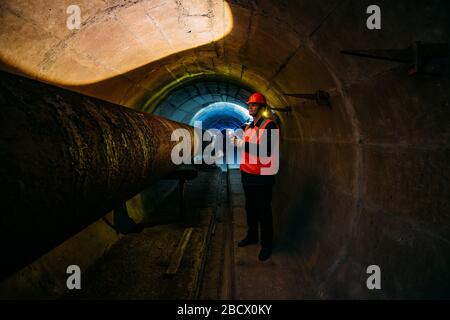 Le travailleur du tunnel examine le pipeline dans le tunnel souterrain Banque D'Images