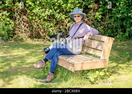 Issaquah, Washington, États-Unis. Photographe féminin portant un appareil photo reflex numérique sur une sangle, assis sur un banc de parc au lac Sammamish Park, Issaquah, Washingto Banque D'Images