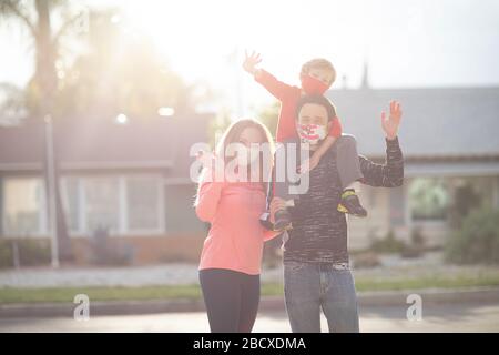 Famille en masques de visage debout dans les quartiers, agitant, saluant. De nombreux pays recommandent aux citoyens de couvrir leurs visages pendant le coronavirus mondial Banque D'Images