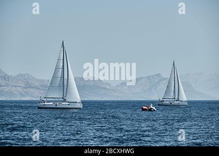 Le bateau en caoutchouc des organisateurs d'une régate avec le juge et ballon de couleur orange, la course des voiliers, concurrence intense, île avec Banque D'Images