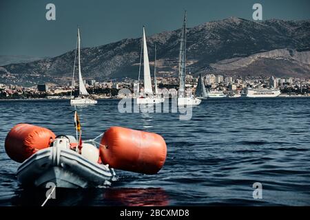 Le bateau en caoutchouc des organisateurs d'une régate avec le juge et ballon de couleur orange, la course des voiliers, concurrence intense, île avec Banque D'Images