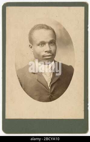 Photographie d'un homme portant un costume et une cravate. Une photo de carte d'armoire noir et blanc d'un homme dans un costume de couleur sombre avec une cravate sans serrer attachée autour de son cou. Il a une moustache. La photo est de forme ovale et collée au Bristol vert. Il n'y a pas d'inscriptions. Photographie d'un homme portant un costume et une cravate Banque D'Images