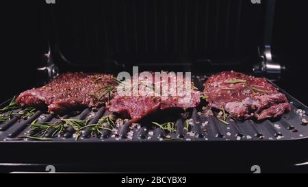 Délicieux bifteck de viande juteuse sur le gril. Faire cuire au bœuf à la sauce au roaster électrique, au romarin, au poivre noir et au sel. Ralenti. Banque D'Images