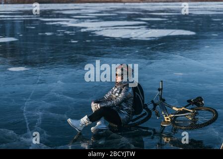 Femme assise près de son vélo sur glace. La jeune cycliste s'est arrêtée de se reposer. Elle se trouve sur la roue et bénéficie de la vue magnifique sur le coucher du soleil. Banque D'Images