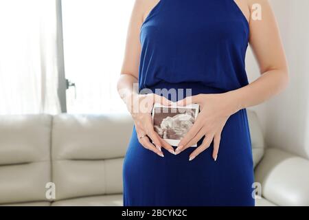 Image recadrée de la jeune femme enceinte tenant l'image échographique du bébé devant son ventre Banque D'Images
