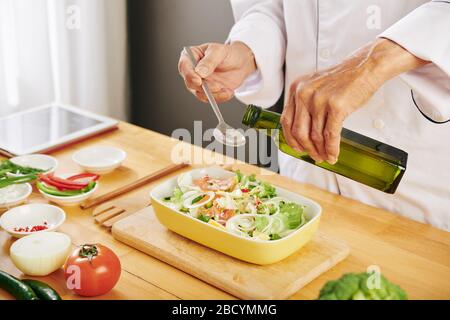 Faire cuire en ajoutant une cuillère de table d'huile d'olive dans un bol de salade fraîche et délicieuse Banque D'Images