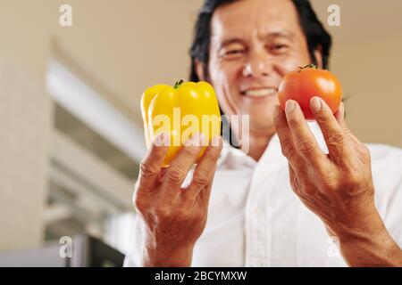 Homme asiatique souriant prenant du poivron jaune frais et de la tomate pour faire de la salade de vitamine Banque D'Images