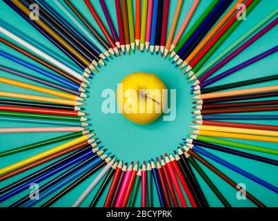 Les crayons de couleur sont disposés dans un cercle et une pomme sur fond bleu Banque D'Images