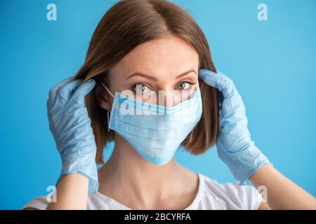 Infirmière ou médecin avec masque et gants. Soins de santé, chirurgie. Gros plan portrait de la jeune femme caucasienne modèle sur fond bleu Banque D'Images