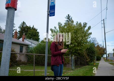 Une jeune fille attend le bus bleu. Le système de transport public dans ce quartier est généralement à l'heure, mais cette fois, il a été retardé. Banque D'Images