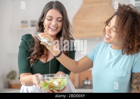 Deux femmes ajoutent de l'huile de salade dans la salade de légumes. Banque D'Images