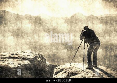 Photographe professionnel sur trépied sur falaise et travail dur. Rêve fogy paysage bleu misty lever de soleil dans une belle vallée sous le filtre de calotype. O Banque D'Images