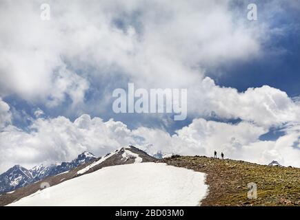 Deux randonneurs en silhouette avec des sacs d'escalade sur la montagne avec de la neige en fond de ciel nuageux Banque D'Images