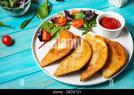 Cuisine latino-américaine, mexicaine et chilienne. Pâtisseries traditionnelles épanadas avec viande de bœuf sur fond bleu en bois Banque D'Images