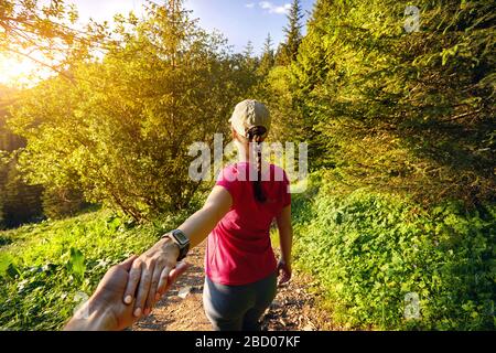 Belle fille sportive en rose shirt homme tenant à la main et le conduisant à la piste de montagne au coucher du soleil Banque D'Images