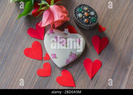 Coeur en porcelaine avec fleurs sur la table de texture en bois avec fleur rose et beaucoup de coeurs en papier rouge autour. Mariage ou signe d'amour. Pose plate. Banque D'Images